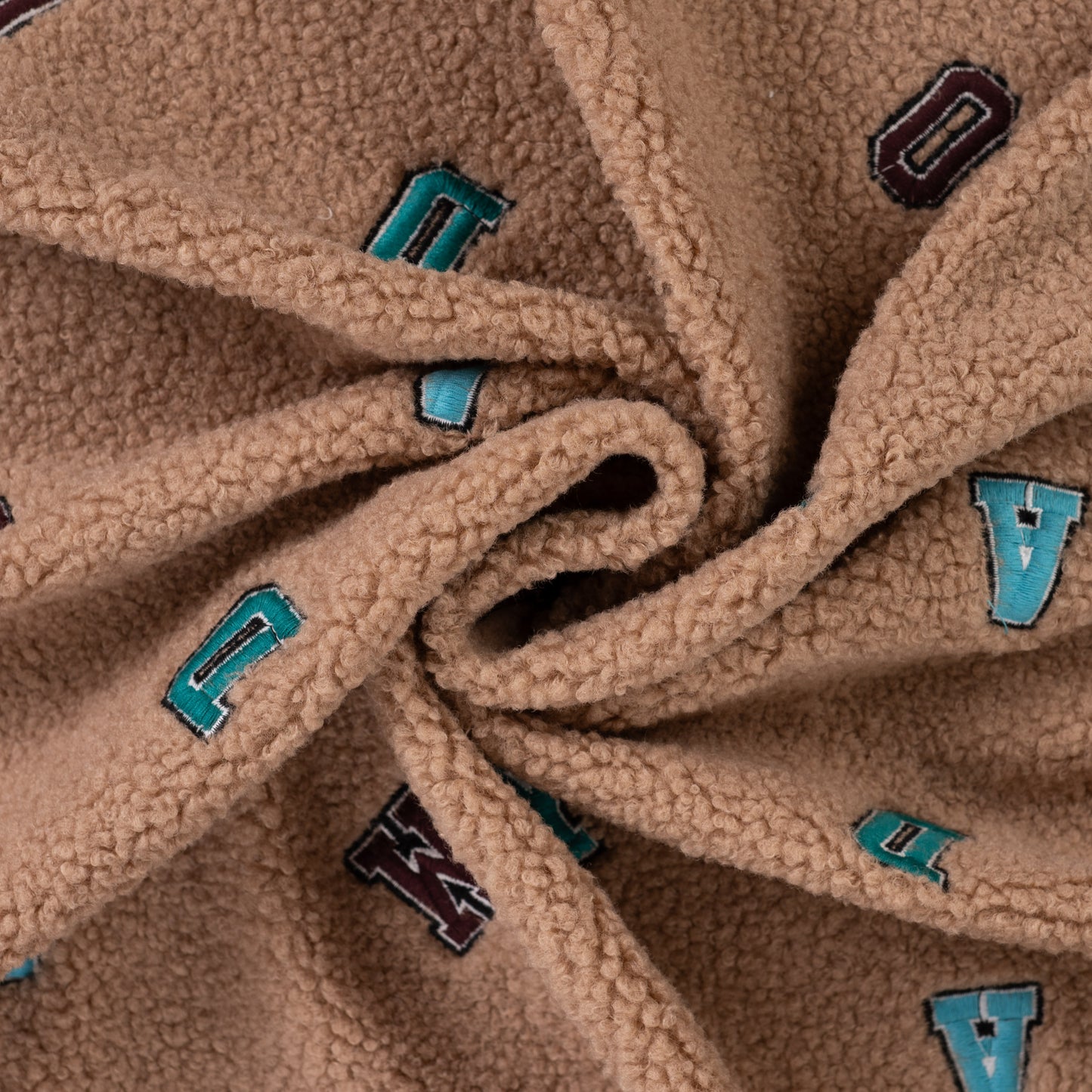 Boucle teddy stof in de kleur lichtbeige met gekleurde letters.