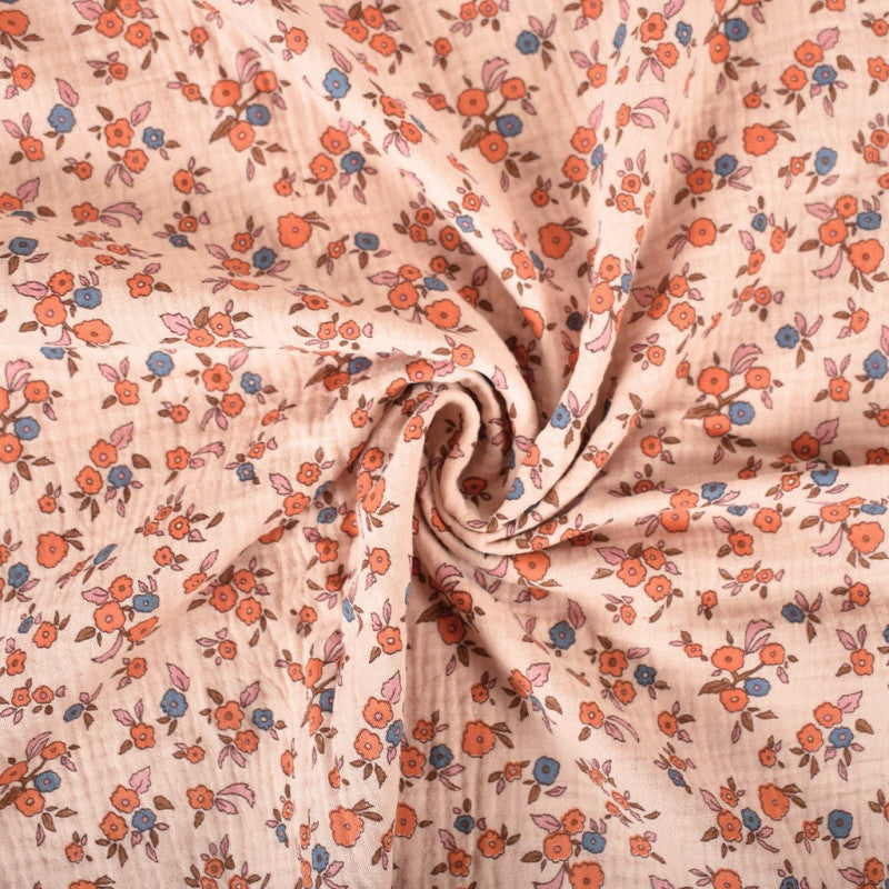 Licht oranje mousseline stof met kleine oranje en blauwe bloemetjes, voor het maken van bijvoorbeeld een jurk of rok voor een meisje of een zomerse broek of blouse.