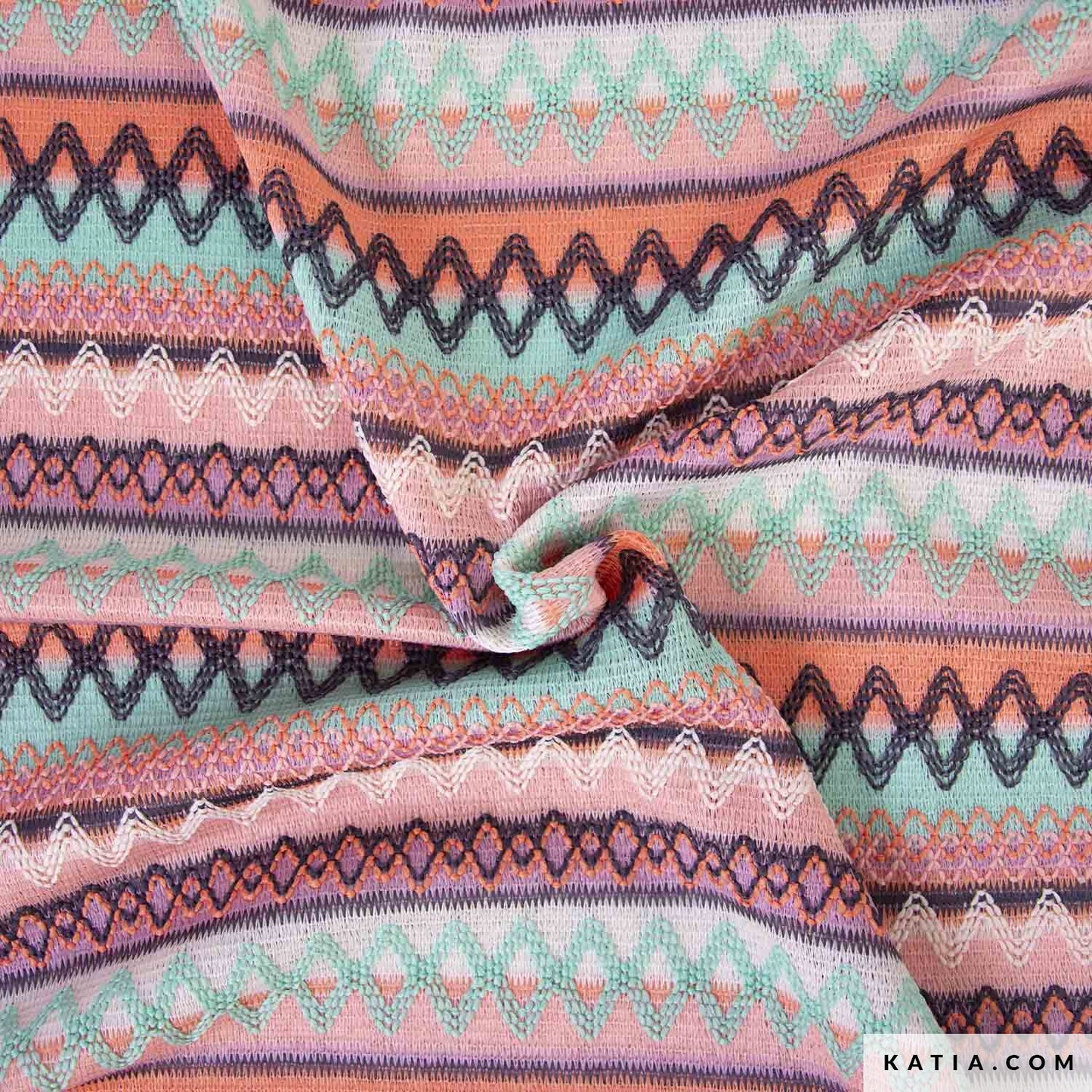 Geborduurde stof met geometrische print in de kleuren roze oranje en groen.